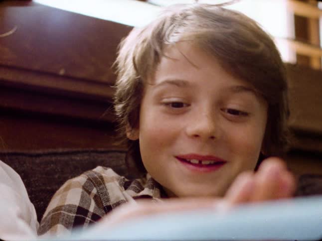 A heartwarming close-up from vintage film shows a delighted young boy smiling as he reads a book with someone