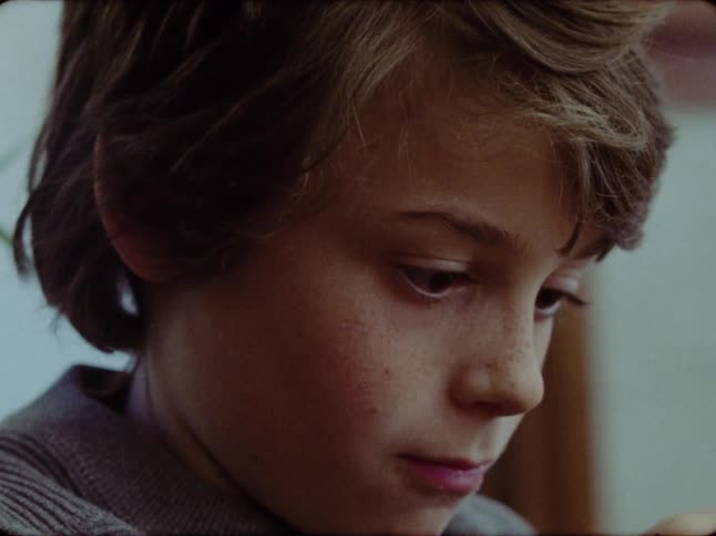Close-up portrait of a thoughtful young boy indoors looking down before meeting the camera