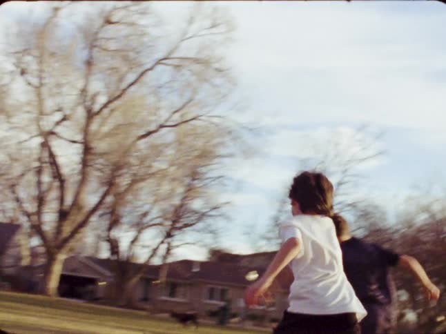 Dreamy 8mm vintage footage shows two young boys energetically playing soccer together in a sun-drenched park