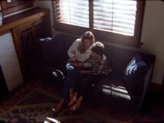 Nostalgic vintage footage captures a tender moment between a mother and son as they read together on a couch in a sunlit room
