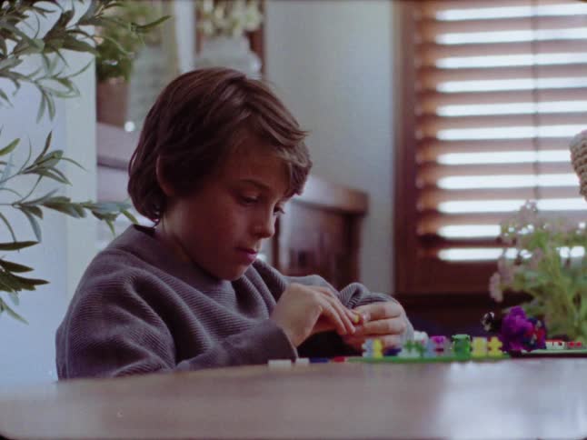 Vintage film captures a young boy with brown hair concentrating as he builds with a colorful construction toy set at a table