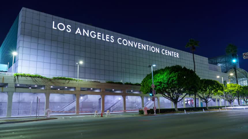 A nighttime time-lapse shows streaks of light from traffic passing the illuminated Los Angeles Convention Center