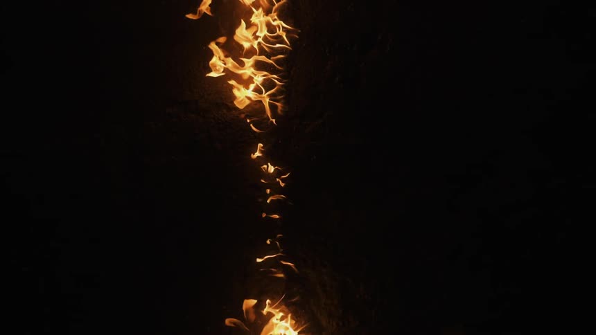 A line of flames ignite and burn in darkness