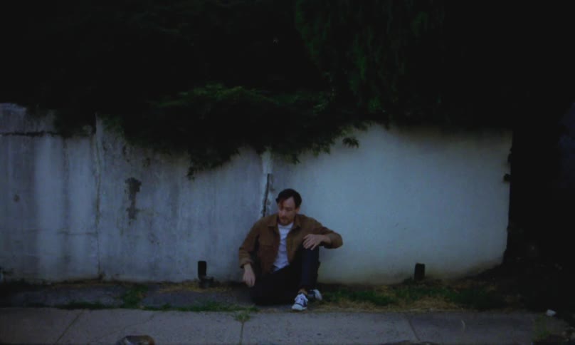 An anxious man walks down the street and sits on the ground