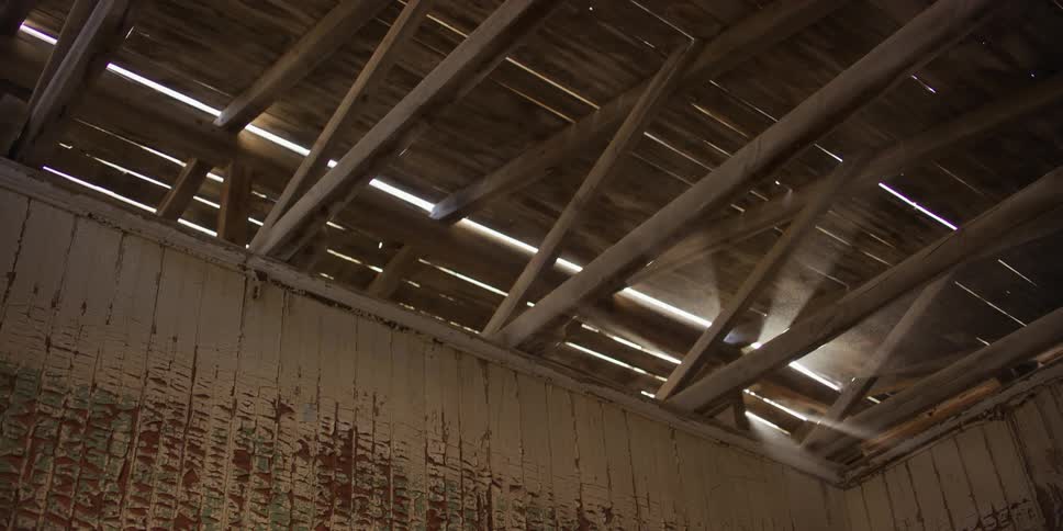 Sunlight streams through the old wooden rafters of an abandoned building, illuminating the dust particles in the air