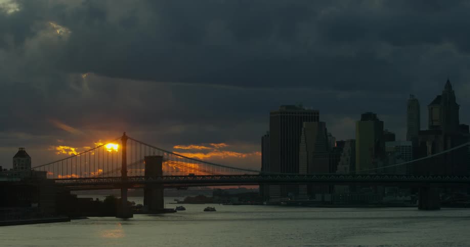 A cloudy sunset behind a suspension bridge in a city