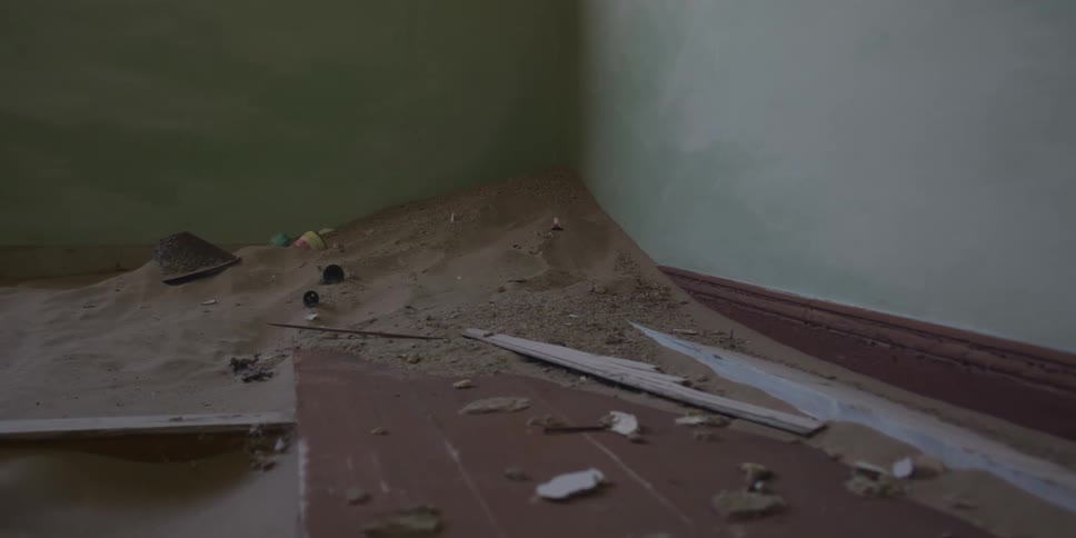 A slow zoom reveals sand dunes forming inside a derelict house, burying forgotten toys and debris