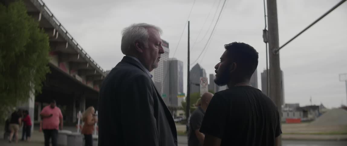 Two men talk on a city sidewalk