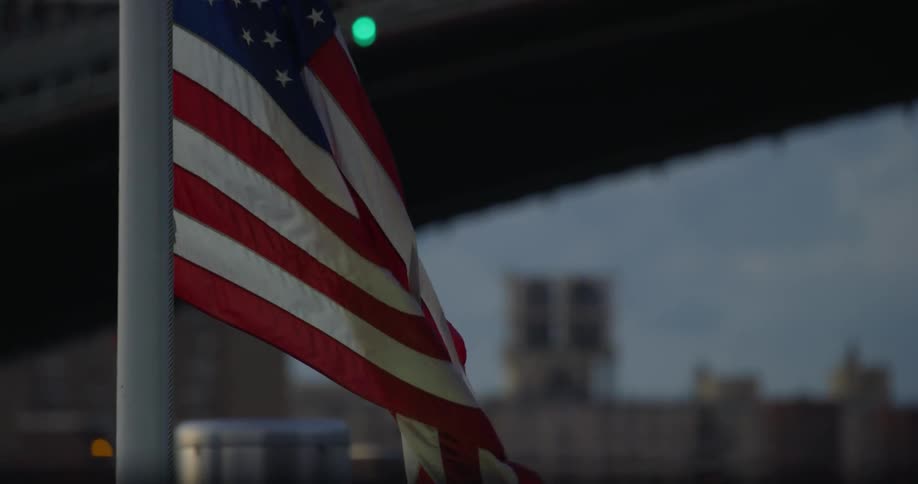 American flag waves in front of a bridge