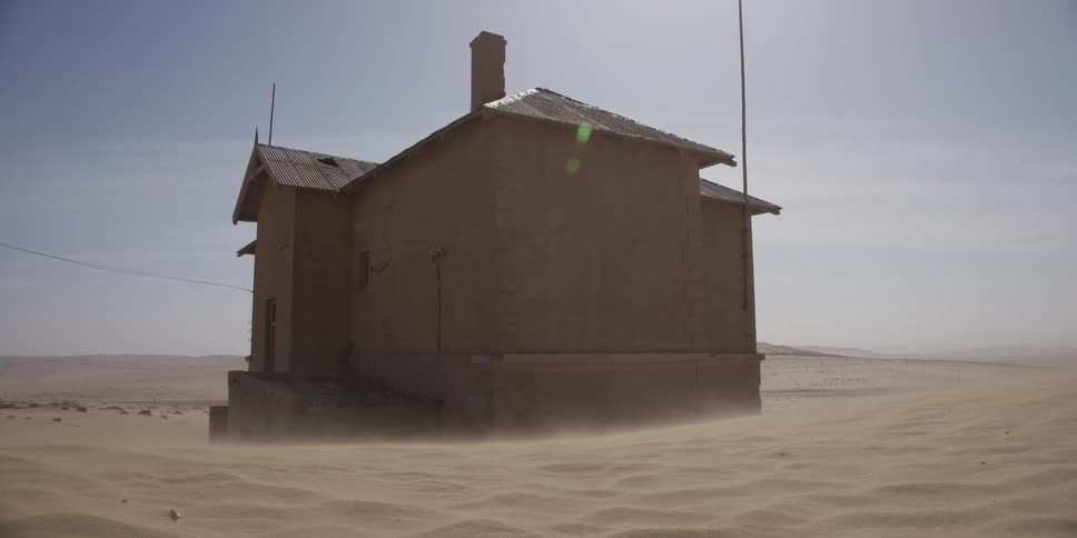 A slow zoom out shot of an abandoned desert house being slowly buried by blowing sand during a windstorm