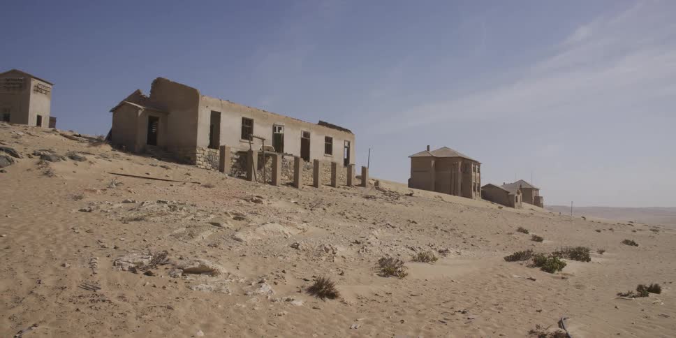 Slow pan reveals abandoned, sand-covered buildings in the desolate ghost town of Kolmanskop, Namibia