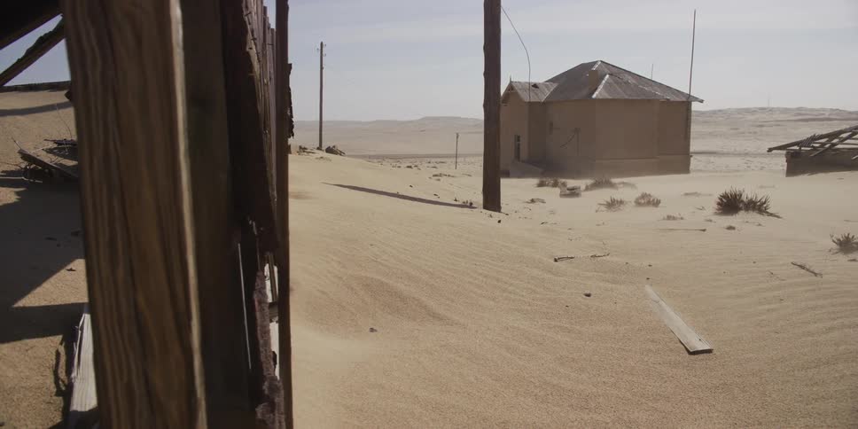 Slow dolly reveal of a desolate, abandoned ghost town being reclaimed by the desert during a powerful sandstorm
