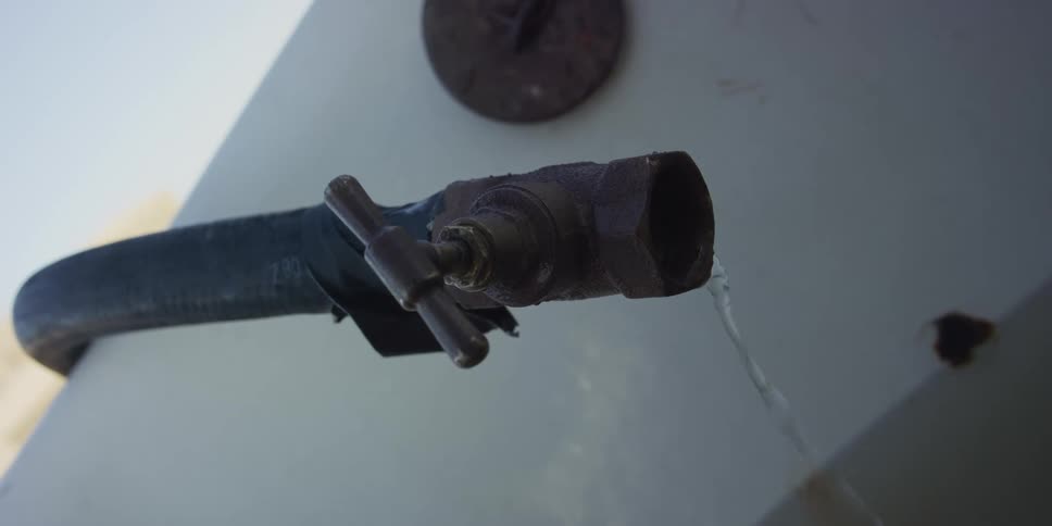 A steady stream of water leaks from a rusty, old outdoor spigot