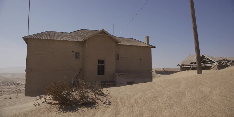 Strong winds sand across the desert landscape, partially burying an abandoned building in a ghost town