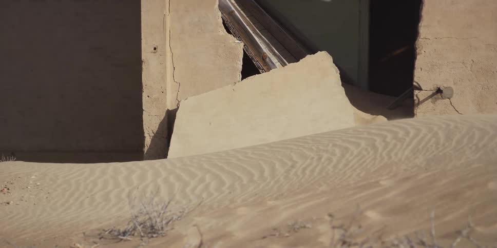 Rippled sand dunes slowly encroach on a dilapidated building in an abandoned desert ghost town