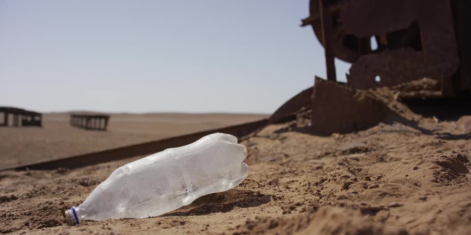 A close-up of a plastic water bottle discarded as litter on the sand in a barren desert