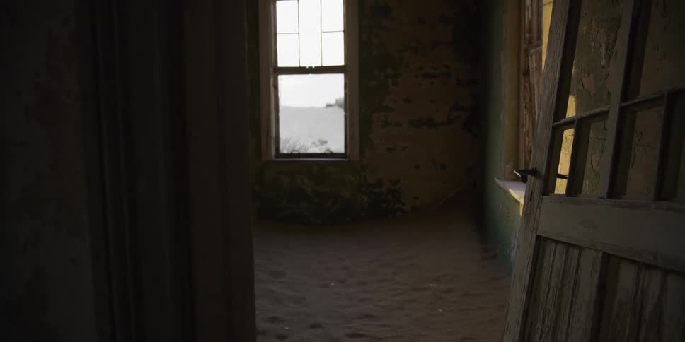 Walking through a doorway into a decaying room reclaimed by desert sand