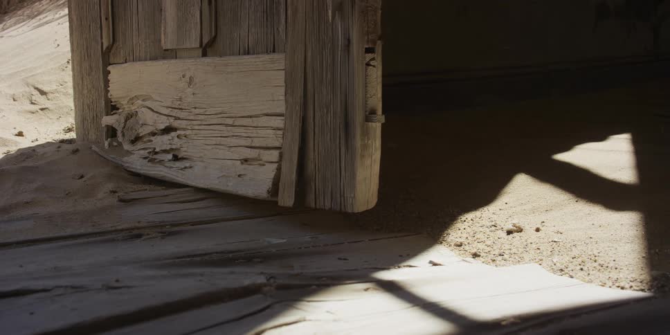 Wind blows desert sand across a wooden floor and through the doorway of a weathered, abandoned building