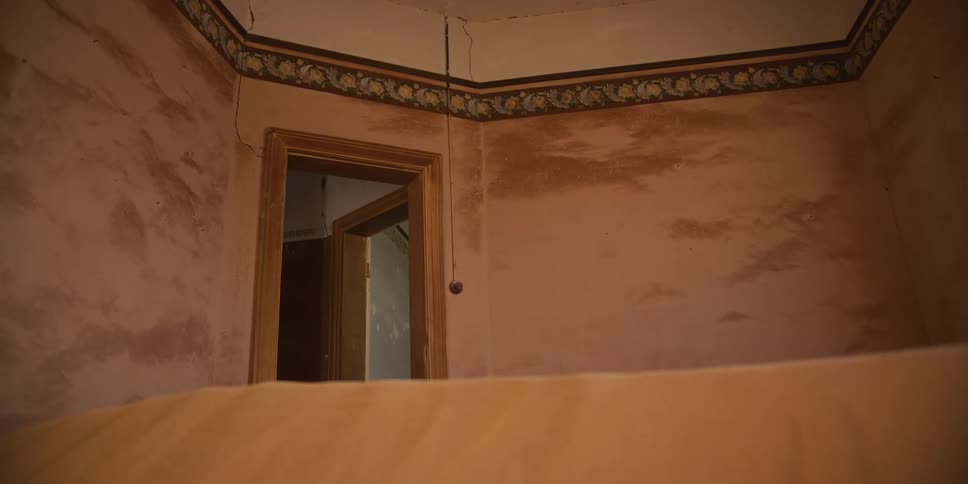 Desert sand dunes fill the interior of an abandoned, decaying room in a ghost town
