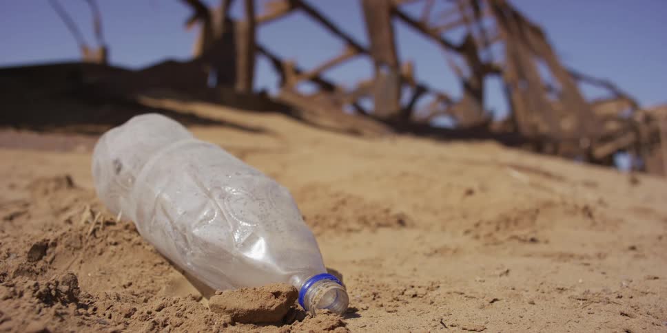 A close-up shot of a single-use plastic water bottle discarded in the sand of a desolate, arid landscape