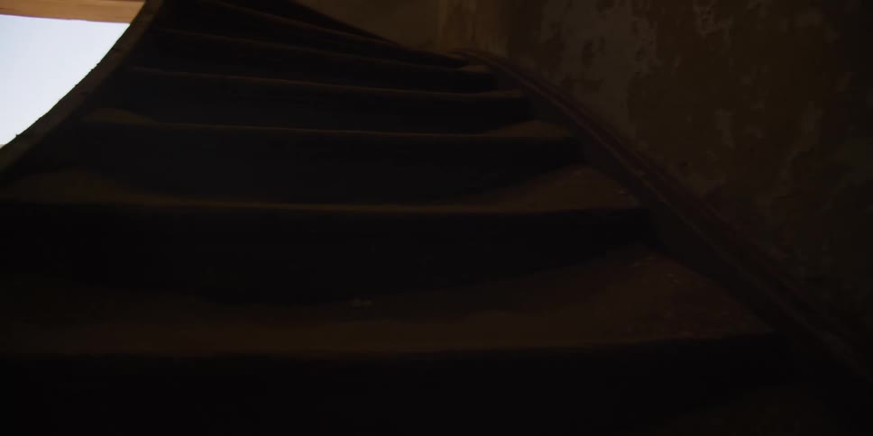 A slow pan reveals the interior of a dark, eerie abandoned house where desert sand has completely filled the rooms and covered the staircase