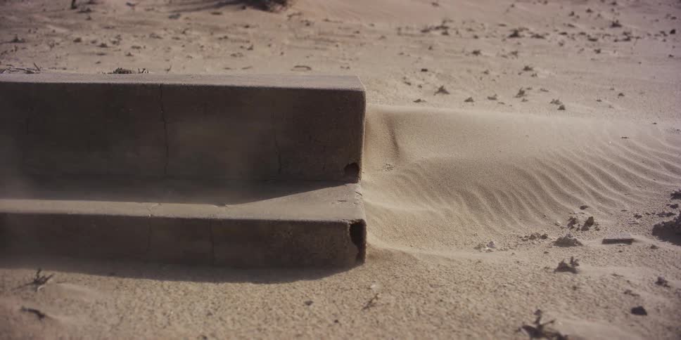 Strong wind blows fine sand over concrete steps creating small drifts in a desolate landscape