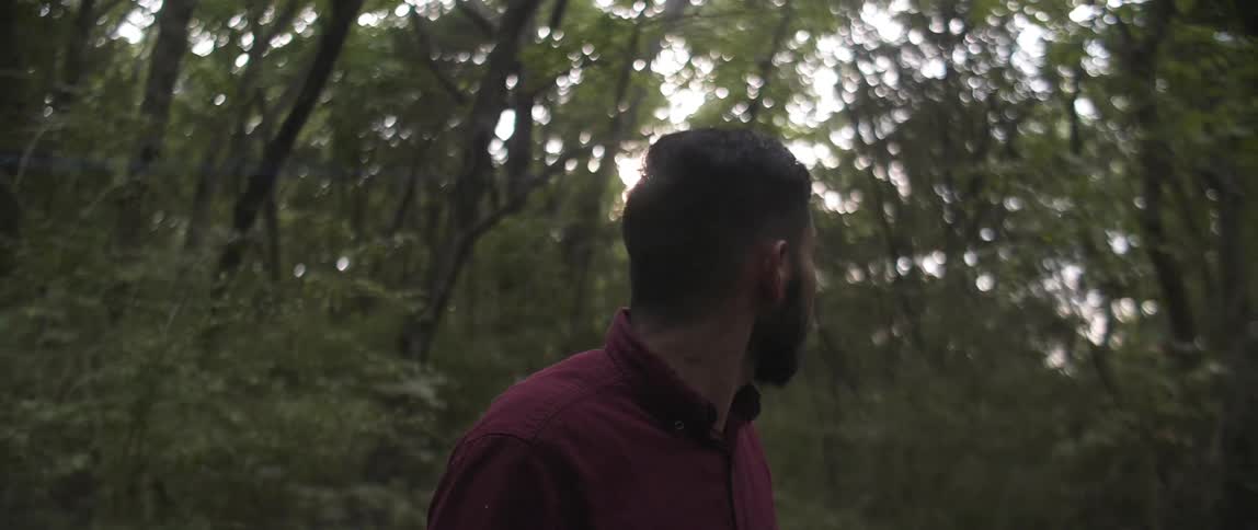 A man walks through a wooded area with the sun shining overhead