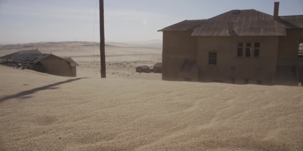 Wind blows sand across the shifting dunes that are slowly burying an abandoned desert ghost town