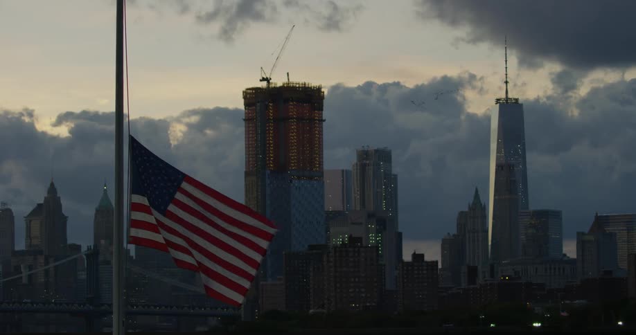 American flag at half mast waving in the breeze in front of city buildings
