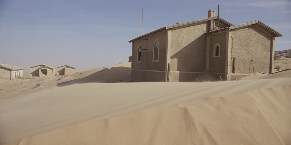 Wind sweeps across the desert, slowly burying an abandoned building under shifting sand dunes
