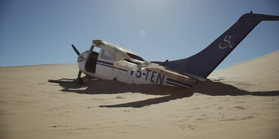 The wreckage of a crashed airplane is partially buried in the shifting sands of a vast desert