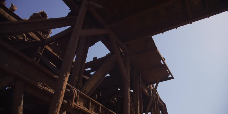 Low angle slow pan reveals the decaying and heavily rusted skeleton of an abandoned industrial building against the bright sky