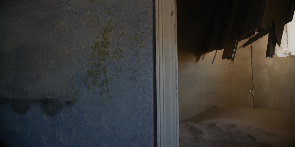 Static shot of the interior of an abandoned house in the desert, with a room filled with sand