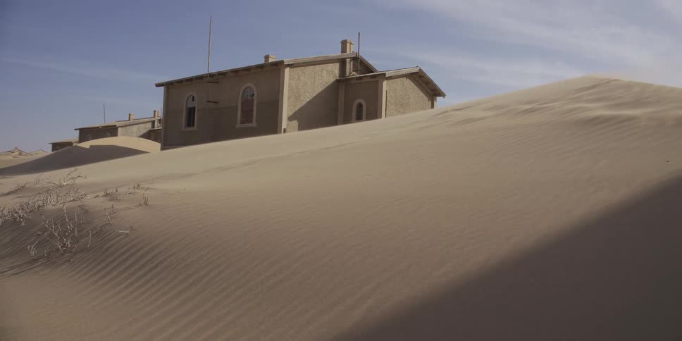 A desolate building in a desert ghost town is slowly being swallowed by shifting sand dunes as the wind blows