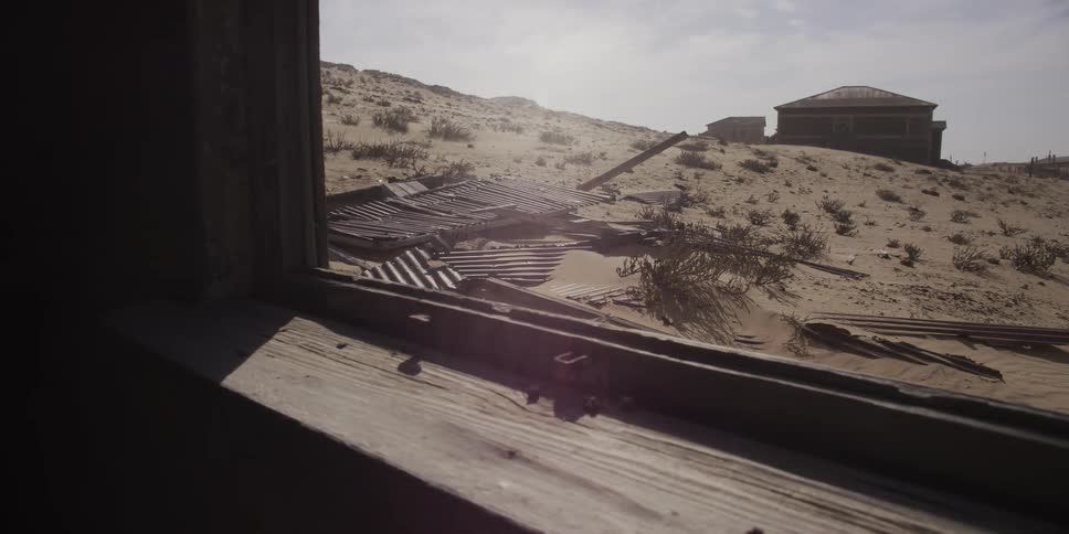 Dolly shot along a dusty windowsill reveals the sun-bleached ruins of an abandoned desert town