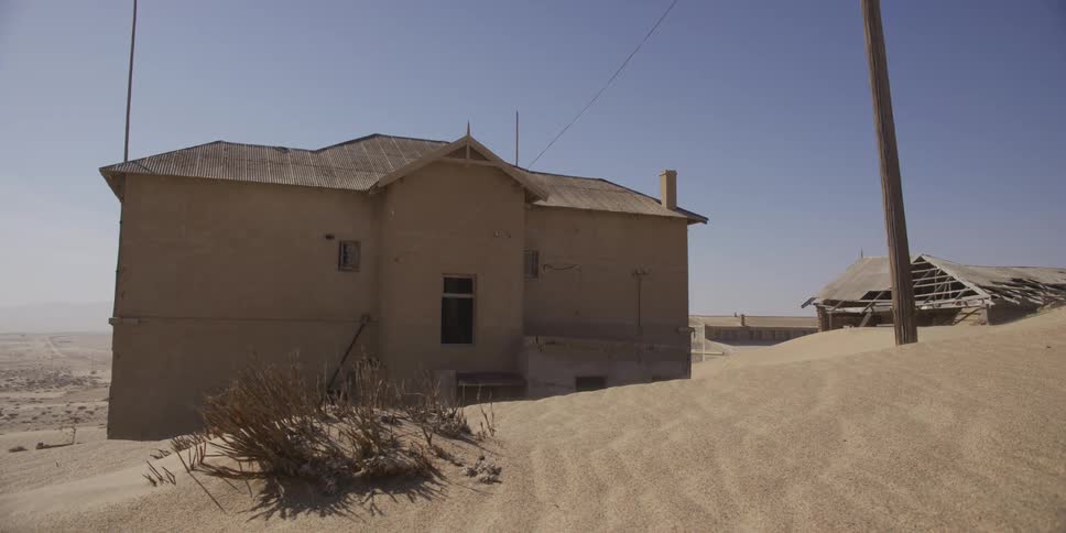 An old, abandoned house in a forgotten desert ghost town stands against the encroaching sand under a harsh sun