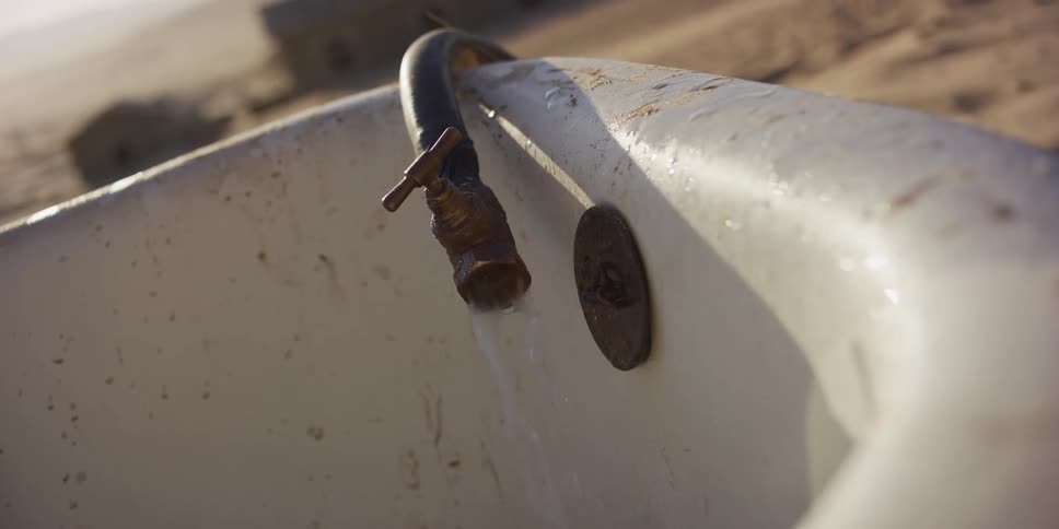 Close-up of a rusty faucet dripping water from an abandoned bathtub in the middle of the desert
