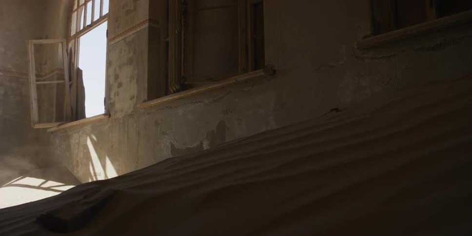 Strong winds sand through an open window into a desolate, abandoned building filled with dunes