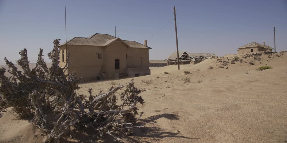 A slow dolly shot reveals the abandoned ghost town of Kolmanskop in Namibia as the wind blows desert sand across the desolate landscape