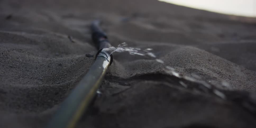 A close-up slow-motion view of water leaking from a broken pipe onto sandy soil