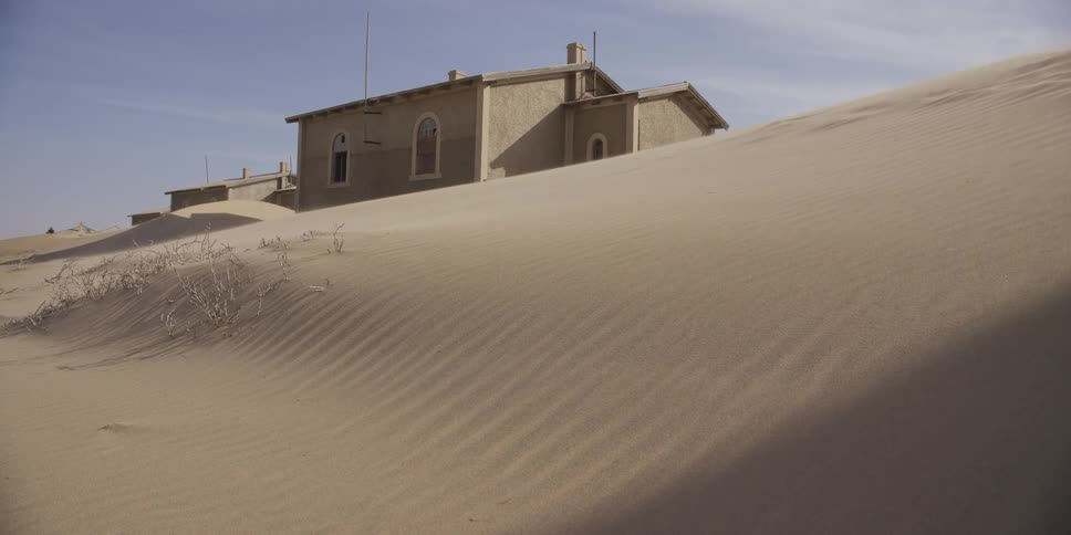 Time-lapse of moving shadows across a desert sand dune slowly burying an abandoned building