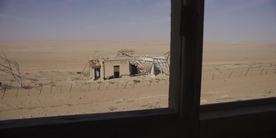 A slow pan reveals a desolate, abandoned building crumbling in the vast, empty desert landscape