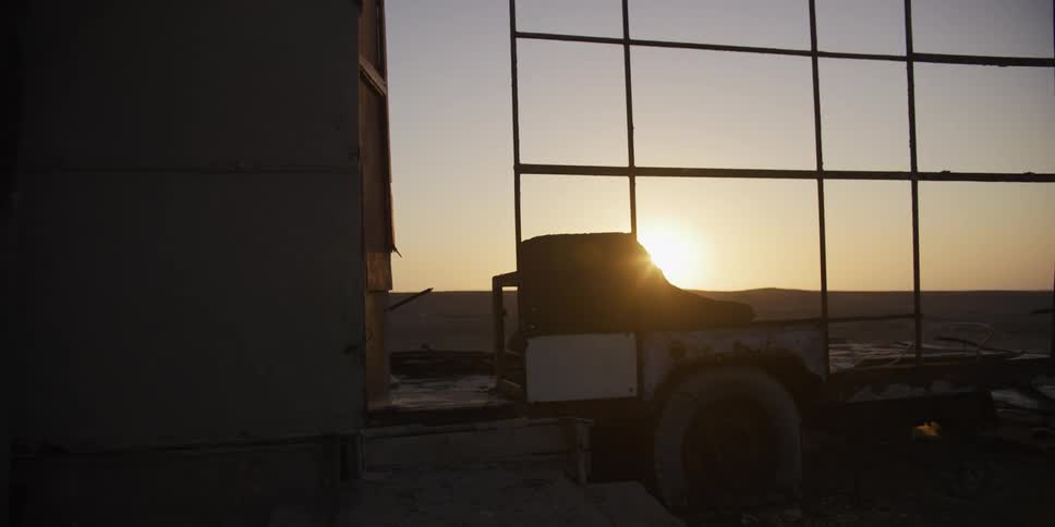 A lone work boot rests on a derelict trailer in a desolate landscape as the camera dollies right at sunset