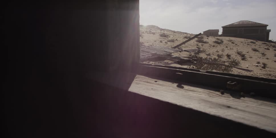 A slow pan from a dark room reveals a sun-drenched, abandoned desert ghost town through a weathered window