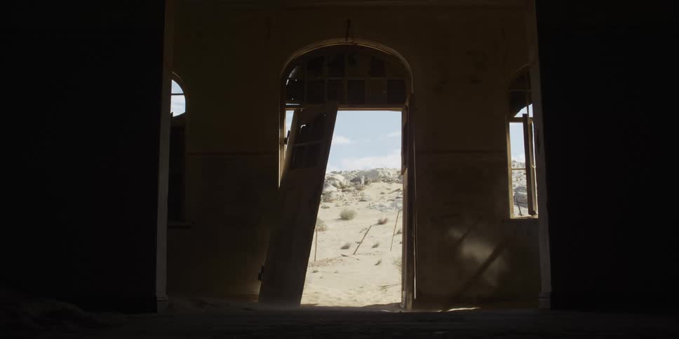 Wind blows sand through the broken door of an abandoned building in the middle of a desert