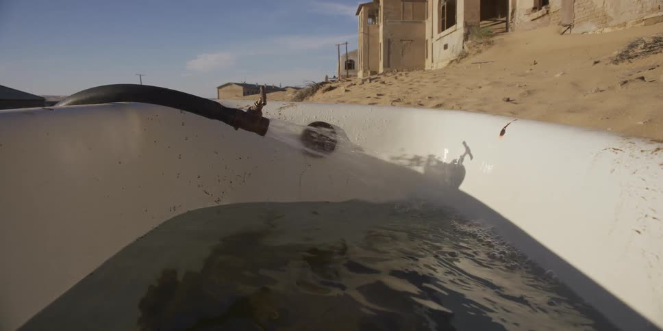 A close-up of water from a hose filling an old bathtub in an abandoned ghost town in the desert