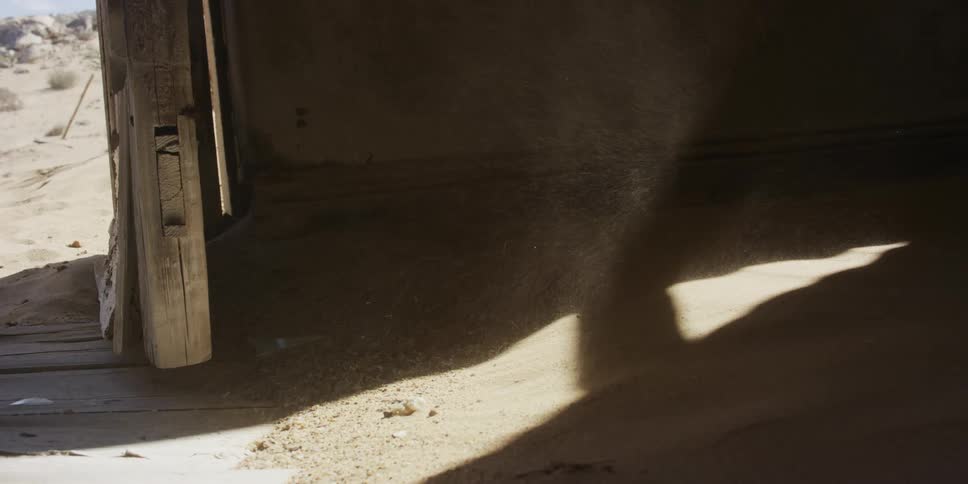 Grains of sand through the cracks of a rustic wooden building during a desert windstorm