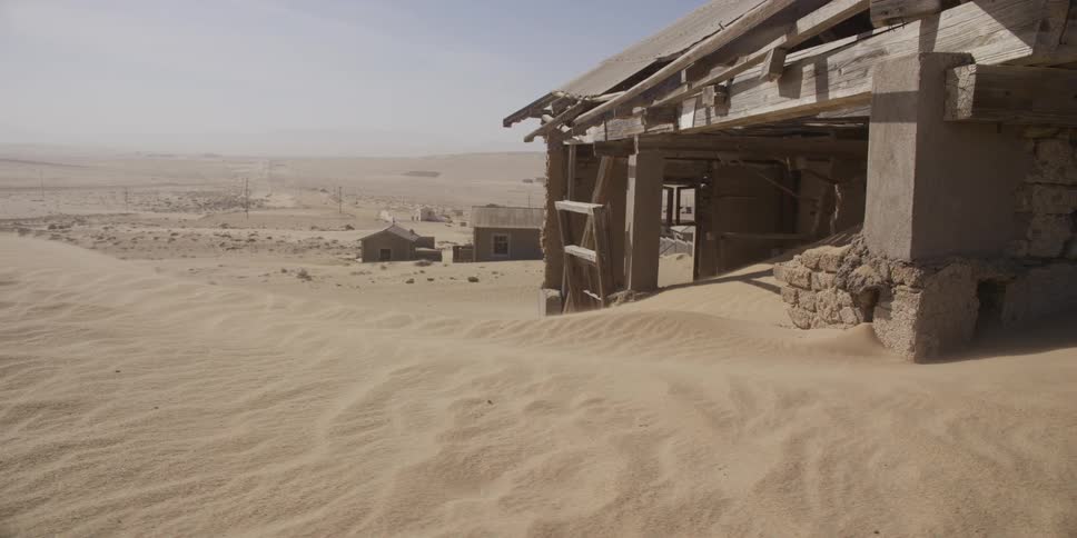 Wind blows sand across a dilapidated building as it is slowly reclaimed by the desert