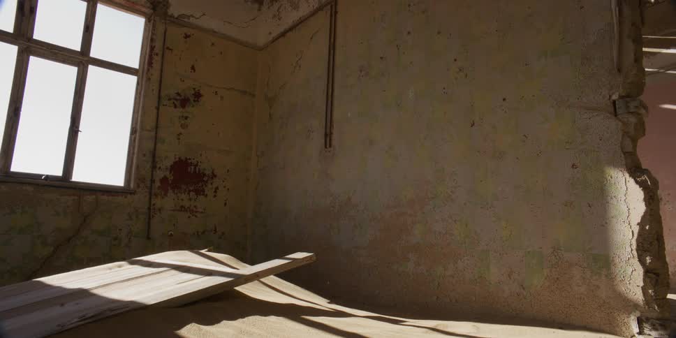 Time-lapse of sunlight casting moving shadows across sand dunes inside an abandoned, dilapidated room in the desert