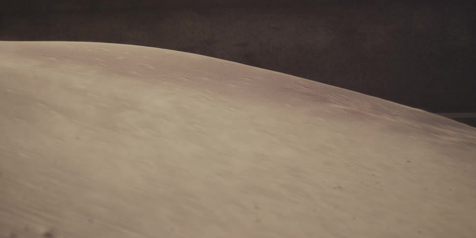 A powerful gust of wind blows sand grains across a large dune in slow motion